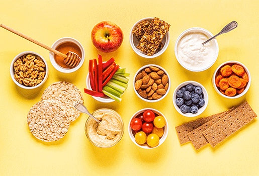 Various snacks (oats, fruit, nuts, vegetables) on a yellow background