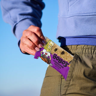 A person putting a Cinnamon Raisin Oat Bar in their pocket, featuring a hand holding a package of oatmeal.