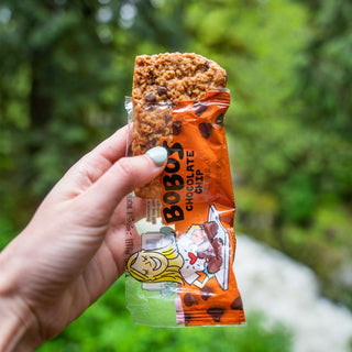 A hand holds a chocolate chip oat bar, a snack made with wholesome oats, coconut oil, and chocolate.