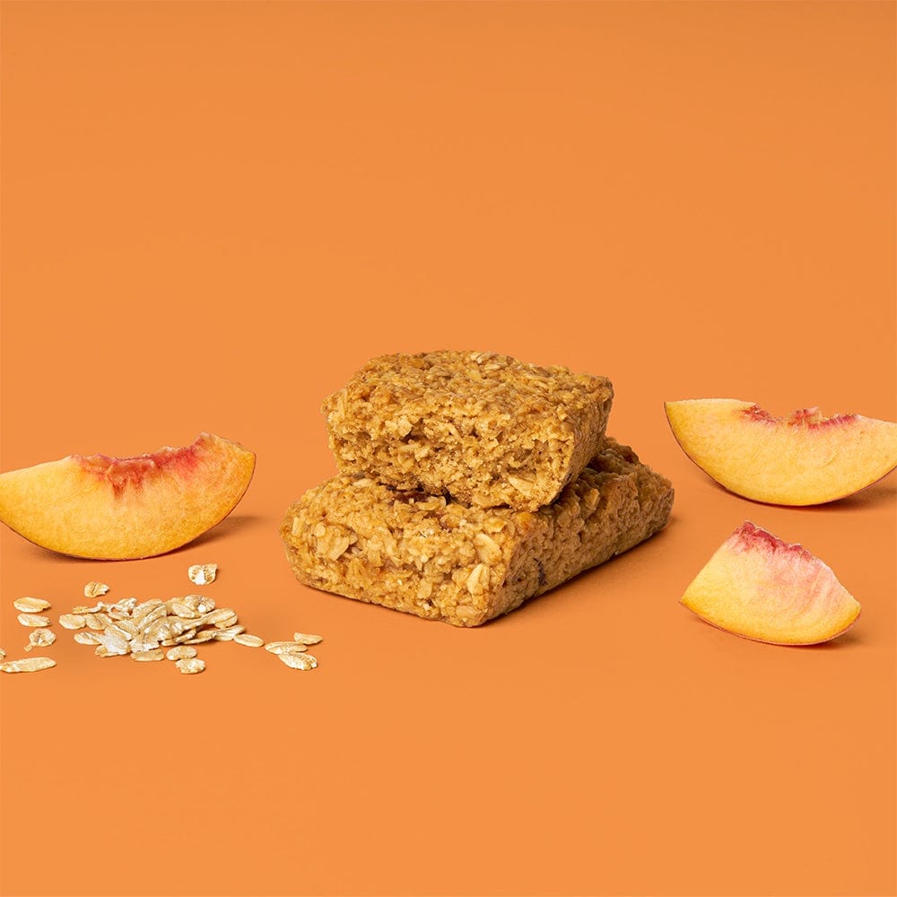 A peach oat bar surrounded by oats, showcasing a slice of peach with a bite taken out.