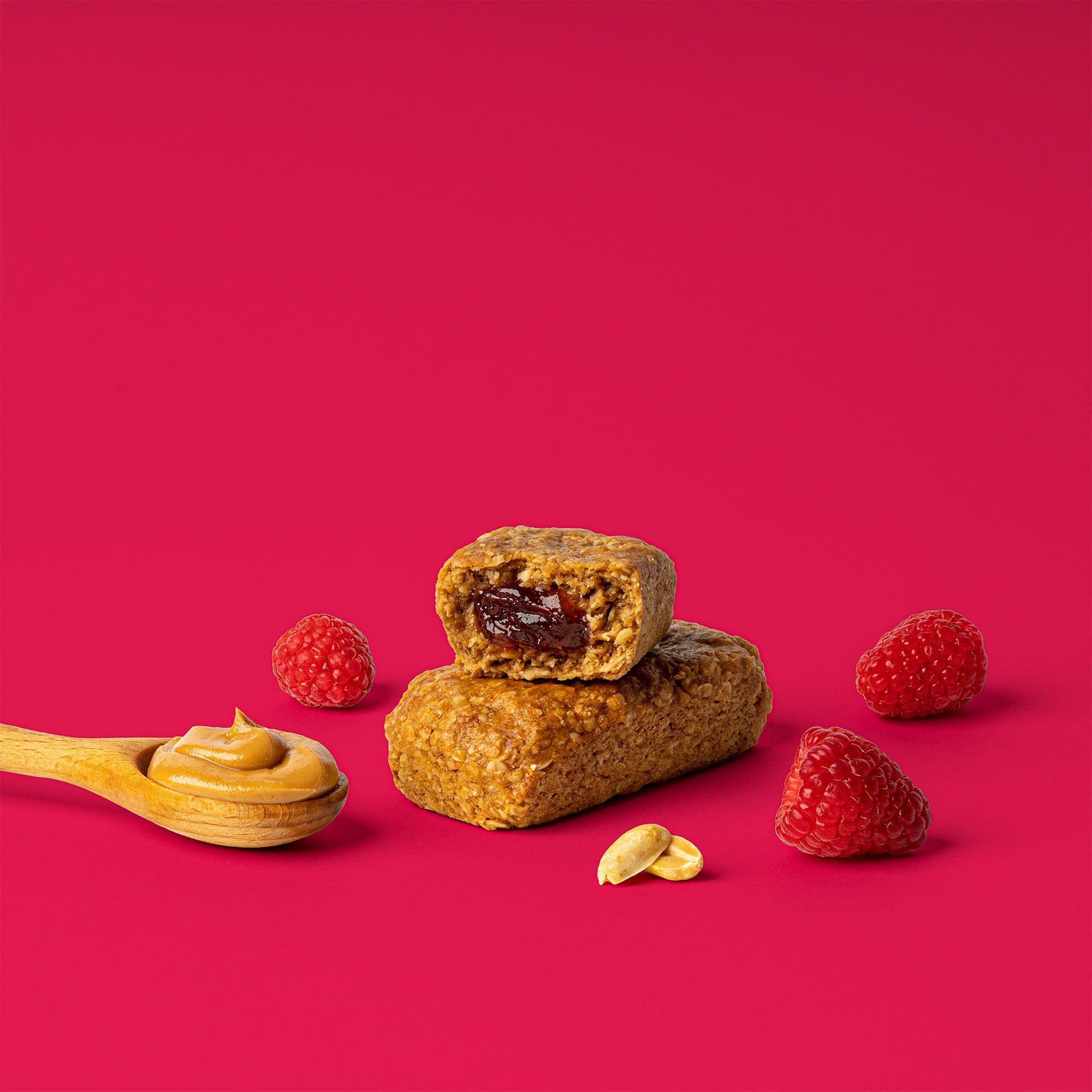 Oat bar on pink background with surrounding peanuts and raspberries