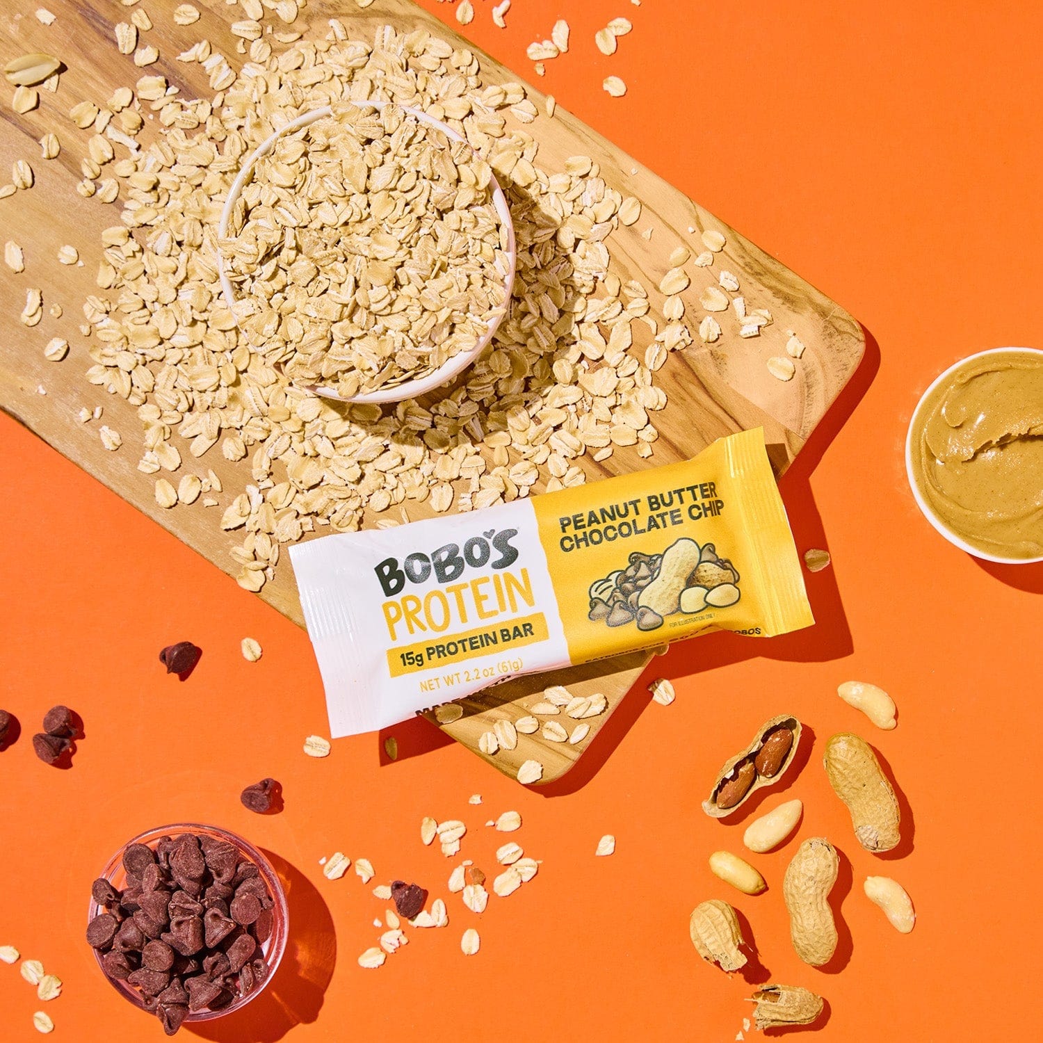 Protein bar on orange background with surrounding chocolate chunks and peanut butter