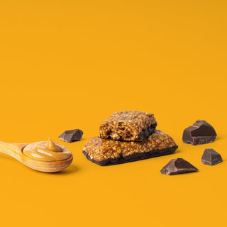 Oat bar on orange background with surrounding chocolate chunks and peanut butter
