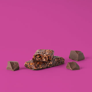 Oat bar on pink background with surrounding chocolate chunks