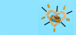 Oats laid out in the shape of a heart with the Peanut Butter Chocolate Chip bar in the center on a light blue backdrop