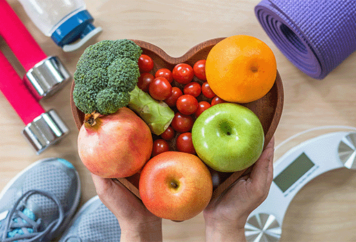 Heart-shaped bowl of fruit surrounded by fitness equipment