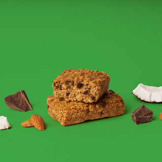 Oat bar on green background with surrounding coconut chunks and chocolate chips