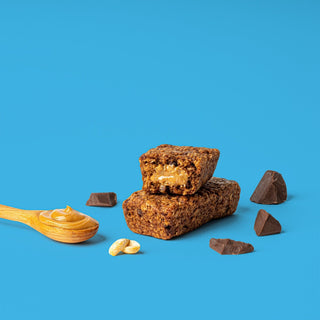 Oat bar on blue background with surrounding peanuts and chocolate chips