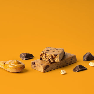 Protein bar on orange background with surrounding chocolate chunks and peanut butter