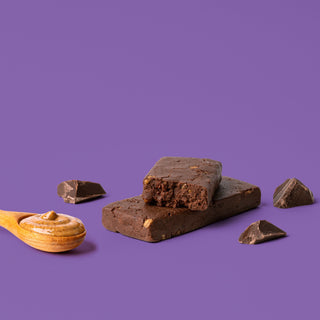 Protein bar on purple background with surrounding chocolate chunks and almond butter