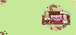 Bobo's Chocolate Almond Brownie Oat Bar displayed on a light green backdrop with oats and chocolate chips scattered